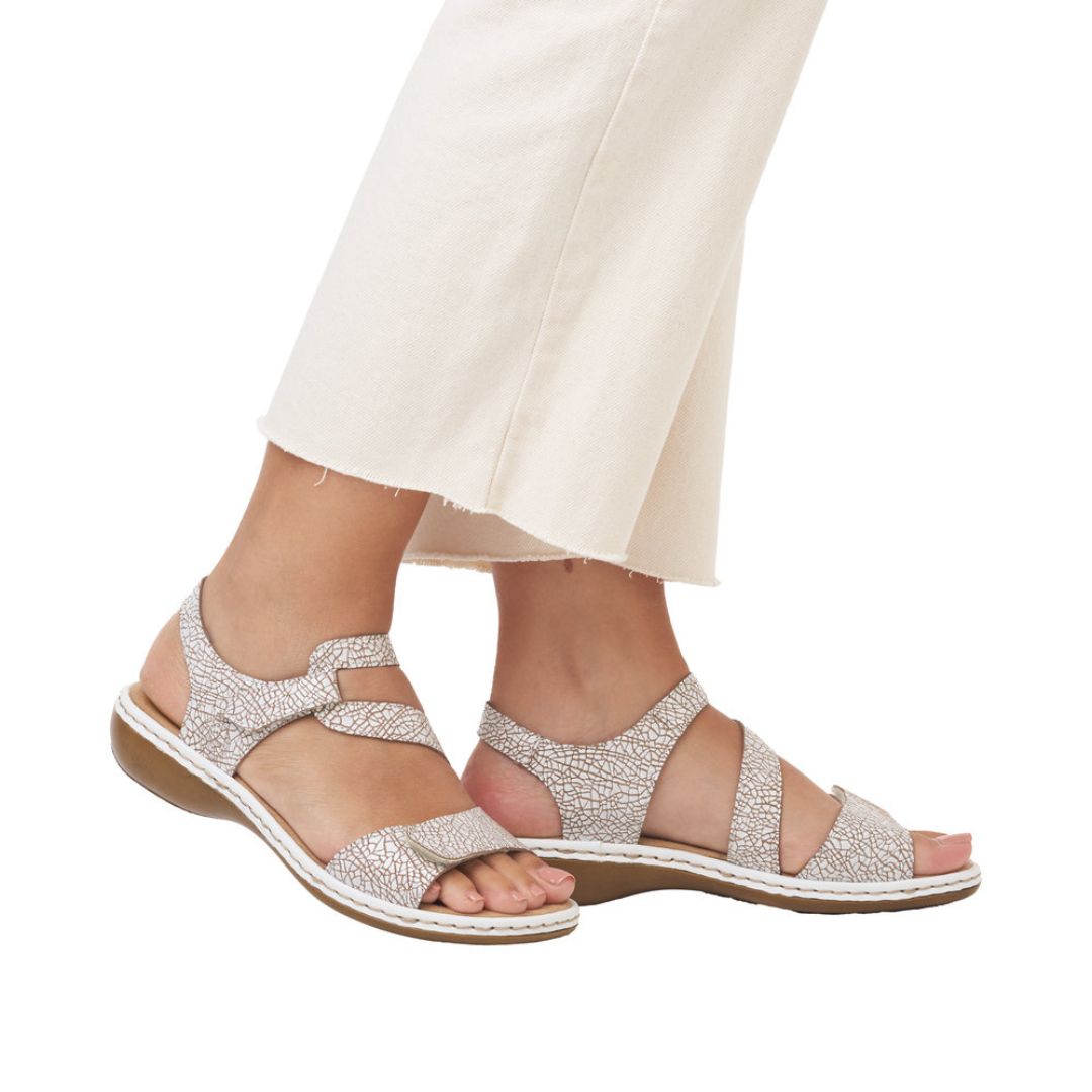 Model wearing white crackle Rieker 659C7 sandals with Velcro straps and cushioned sole, styled with cream pants.