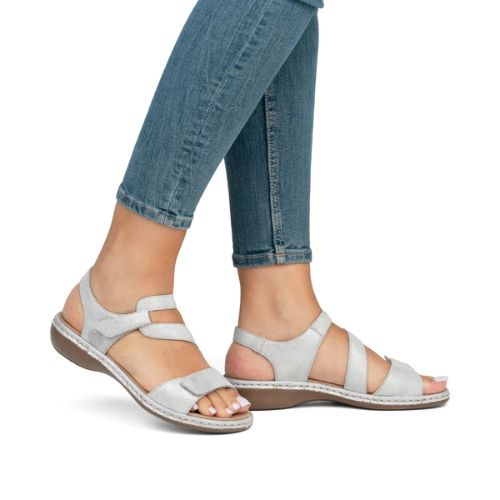 Model wearing silver Rieker 659C7 sandals with Velcro straps and cushioned sole, paired with denim jeans.