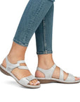Model wearing silver Rieker 659C7 sandals with Velcro straps and cushioned sole, paired with denim jeans.