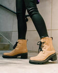 Model wearing Women's Sorel Joan Now Lace Waterproof Boots in tan leather, styled with black skinny jeans for urban fall fashion.