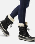 Black Women's Sorel Winter Carnival Waterproof Boots styled with jeans, highlighting mid-calf height and warm fleece lining for winter fashion.