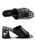 A pair of black open toe leather block heel sandals with a black and white checkered footbed. The block heel has chunky "Z" shaped cut out.