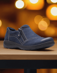 Navy Clarks Carleigh Ray slip-on shoe displayed on a table with warm lighting, ideal for casual women's footwear with comfort and style.