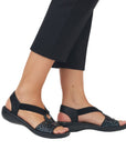 Model wearing black Women's Rieker 60880 Backstrap Sandals with medallion embellishment, perfect for casual summer outfits.