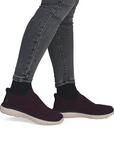 Burgundy slip-on shoes worn with gray jeans and black socks.