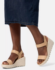 Model wearing Women's Sorel Cameron Wedge Sandal in beige, highlighting the supportive wedge heel and stylish leather straps.