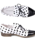 Pair of Women's Oxford shoes in white with black polka dotted leather with black laces, slip on style, black patent toe cap and a low stacked heel.