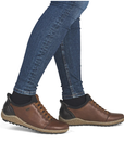 A person wearing blue skinny jeans and brown leather lace-up shoes with black heel accents, shown against a plain white background.