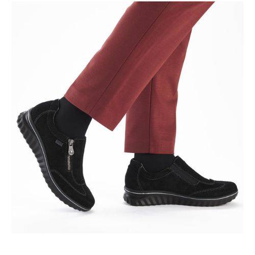 Model wearing Women's Rieker 59071 Slip-On Shoe in black, styled with red pants, showcasing its casual waterproof wedge design.