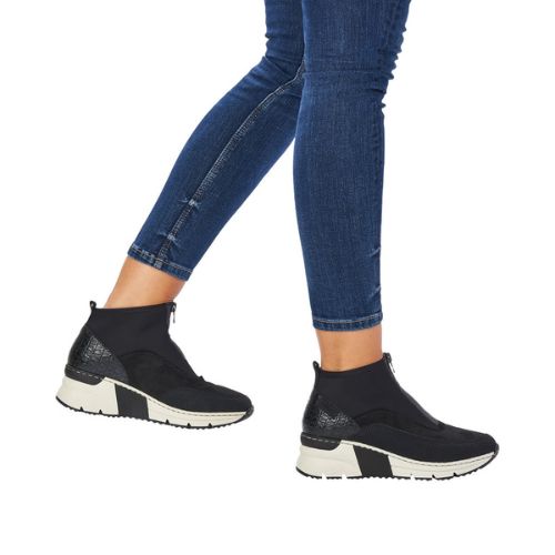 Women in blue jeans wearing black sneaker boots with a white platform outsole.