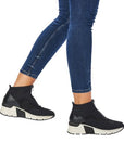 Women in blue jeans wearing black sneaker boots with a white platform outsole.