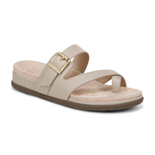 Beige strappy sandal with decorative buckle and toe loop criss-cross straps on a beige suede footbed with black rubber outsole.