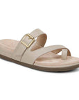 Beige strappy sandal with decorative buckle and toe loop criss-cross straps on a beige suede footbed with black rubber outsole.