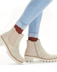 Woman in blue jeans and burn orange socks wearing beige lugged Chelsea boots.