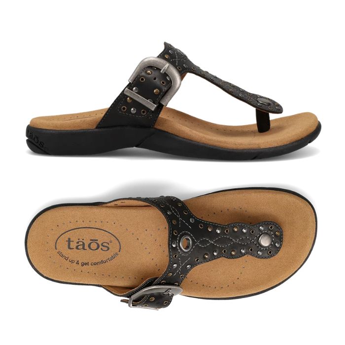 Pair of Black T-strap sandal with embroidery, rivets and grommet detailing and an antiqued adjustable buckle with Taos logo'd beige footbed and black outsole.