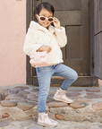 Child wearing a light pink puffer jacket, jeans, and glittery pink leopard print ankle boots standing on stone steps.