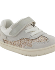 A toddler's light gray sneaker with a glittery gold and silver side panel, white elastic lacing, and a hook-and-loop strap closure.
