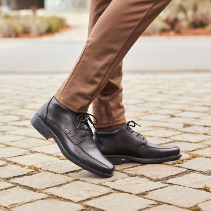 Model wearing Rieker B0011 men's lace-up dress boots with brown pants, showcasing stylish waterproof footwear for fall fashion.