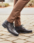 Model wearing Rieker B0011 men's lace-up dress boots with brown pants, showcasing stylish waterproof footwear for fall fashion.