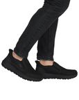 Black slip on sneakers worn with black jean pants.