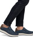 Navy slip-on shoes with brown accents worn with black jeans.