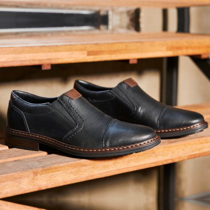 Black Rieker 17659 men's leather dress shoes displayed on wooden steps. Elegant and versatile slip-on shoes for any occasion.