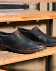 Black Rieker 17659 men's leather dress shoes displayed on wooden steps. Elegant and versatile slip-on shoes for any occasion.