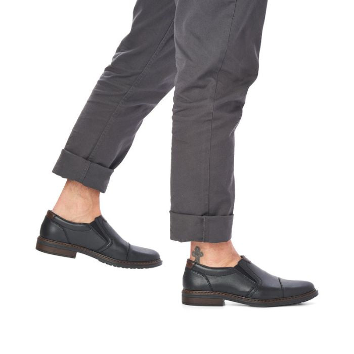 Model walking in black Rieker 17659 leather dress shoes. Comfortable slip-on shoes pair well with jeans or trousers.