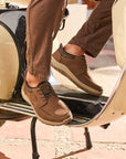 Brown elastic slip on leather sneakers worn by man in brown pants on a scooter