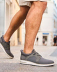 Man wearing beige shorts in a town walking in grey slip on sneakears.