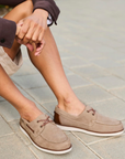 Person wearing brown boat shoes sitting on a stone pathway.