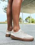 White sneakers with brown accents and outsoles worn by a person standing on a paved surface.