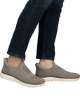 Legs of man in dark jeans wearing beige mesh slip on sneakers with an off white outsole.