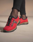 Close-up of red Women's Rieker N3267 Slip-On Sneaker worn with black pants, showcasing stylish design and comfort-focused features.