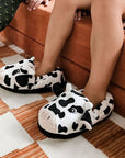 Child sitting on bench with 3D cow slippers on.