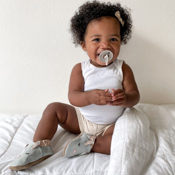 Baby girl playing on mattress with grey leather bunny shoes on.