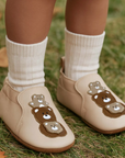 Toddler wearing Soft Sole leather shoes with bear designs and with white socks on a grassy background