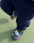 Child's feet wearing navy blue baby shoes with construction vehicle pattern standing on green floor.