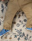 Baby wearing beige pants and blue canvas shoes with vehicle pattern on a patterned rug.