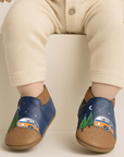 Blue and brown baby's shoes with camper design worn by a child sitting on a beige ledge.