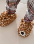 Child in plaid pajamas wearing brown 3D deer fluffy slippers.
