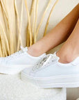 Woman wearing Maya sneakers in white, resting feet on a stool.