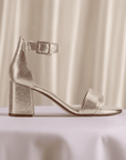 Gold Clarks Ezoria Mae Heeled Sandal displayed on a table with soft draped background, showcasing its wedding-ready elegance.