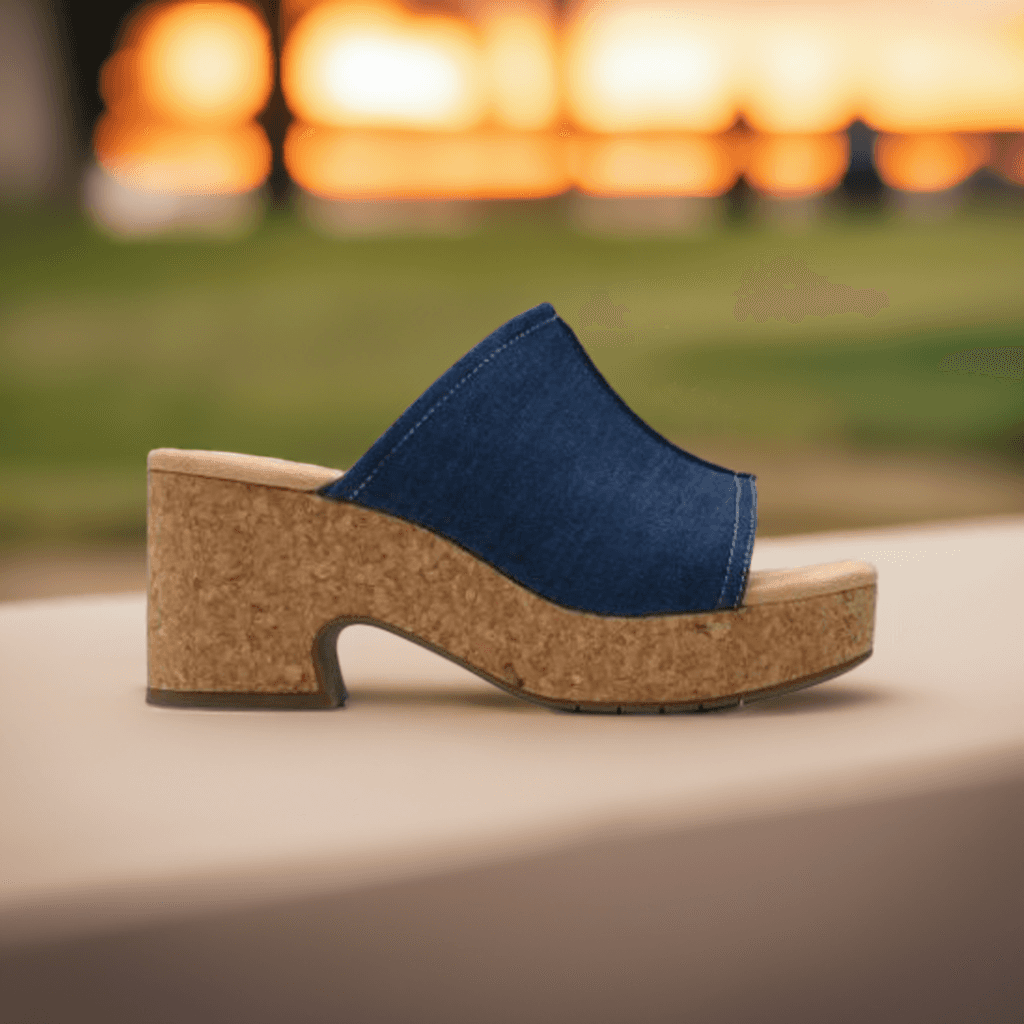 Clarks Nerisa Vine Heeled Sandal in denim blue displayed outdoors at sunset, highlighting its trendy cork platform.