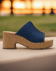 Clarks Nerisa Vine Heeled Sandal in denim blue displayed outdoors at sunset, highlighting its trendy cork platform.