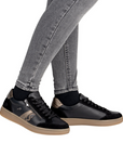 Black sneakers with bronze and cheetah accents and tan soles worn with gray jeans.