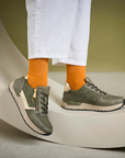 Person wearing green sneakers with orange socks on a neutral background