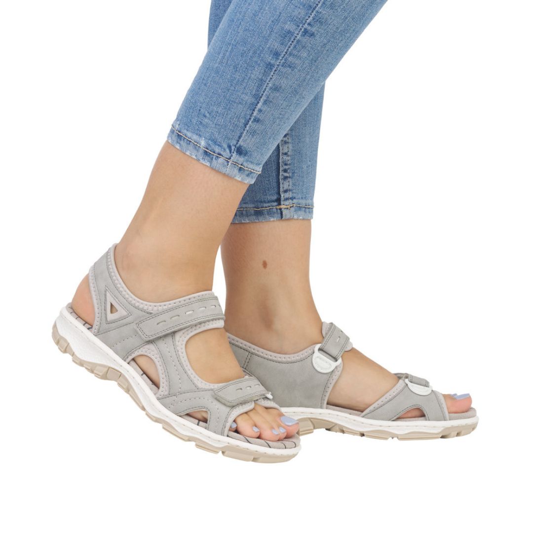 Model wearing Women's Rieker 68866 Backstrap Sandal in grey, styled with jeans, showcasing its supportive fit and casual look.