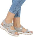 Model wearing Women's Rieker 68866 Backstrap Sandal in grey, styled with jeans, showcasing its supportive fit and casual look.