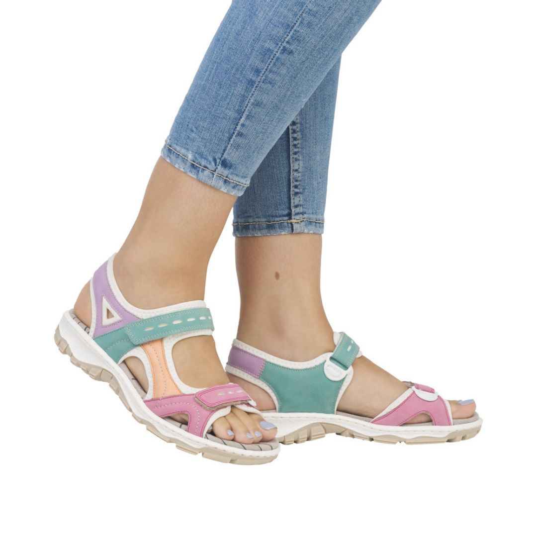 Model wearing multicolor Women's Rieker 68866 Backstrap Sandal with jeans, highlighting its vibrant design and walking support.